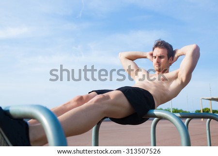 Young muscular build man doing crunch press exercises with copy space area for your text message or advertising content, athletic man warming up outdoors in summer day