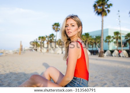 Portrait of a young caucasian woman with beautiful figure posing for the camera while look to you, beautiful female enjoying rest while sitting on the beach in sunny summer evening, cute hipster girl