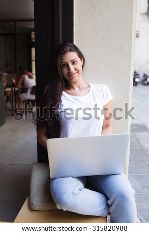 Portrait of charming latin woman using a laptop computer while relaxing in cafe terrace browsing internet, young hipster girl sitting with open net-book while working in a modern coffee shop