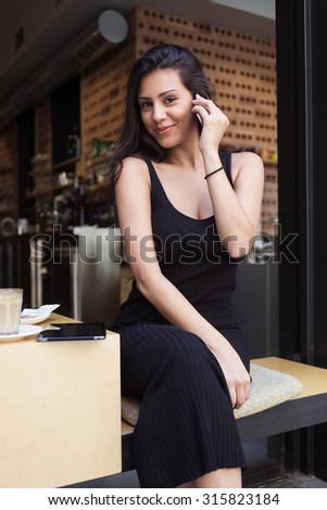 Portrait of a beautiful latin woman looking at the camera during telephone conversation, female student talking on her smart phone while resting after lectures in modern coffee shop in the fresh air
