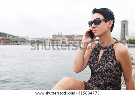 Portrait of a young brunette woman calling with smart phone while enjoying good day outdoors, stylish female tourist talking on her cell telephone while relaxing after walking during summer weekend