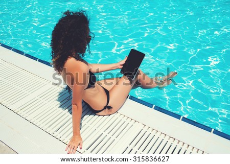 Sexy woman in swimwear using digital tablet for distance work while relaxing near pool during weekend, young bikini model holding touch pad with blank copy space screen for your advertising content