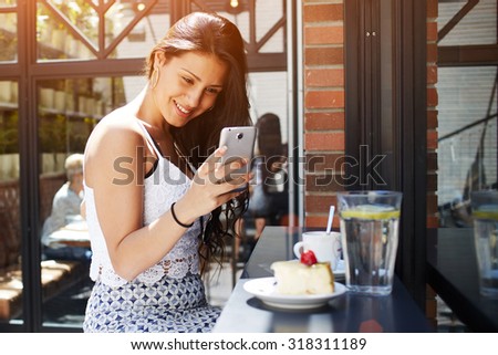 Young attractive female taking picture of her coffee shop breakfast with mobile phone camera, smiling gorgeous latin woman photographing cake with berries on her cell phone, people using technology