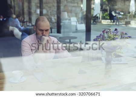 Puzzled and concerned male freelancer or student look to net-book, worried and thoughtful businessman or entrepreneur sitting front open laptop computer in modern coffee shop interior in urban setting