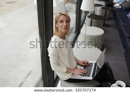 Gorgeous young woman sitting with open laptop computer in modern coffee shop or hotel interior, female freelancer using net-book for her distance work, student girl learning via portable gadget device