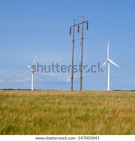 Barley field in the wind, electric wind mills and overhead power lines. Sustainability concept.