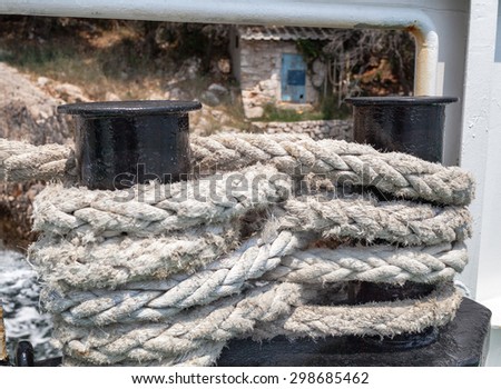 strong nautical rope tied in figure eight around piers aboard a ship; old fisherman\'s cottage in the background;