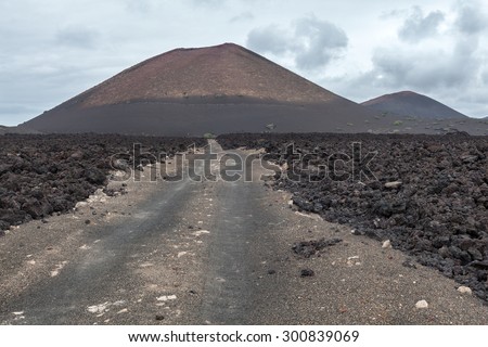 Lanzarote volcanic landscape; Long dirt path leads to the volcano crater; Lanzarote is one of the Canary islands, Spain.