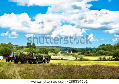 Landscape with haymaking. The tractor and the trailer of hay in a field. Fields and meadows at summer, the idyllic rural landscape and agricultural. Blue sky with clouds and sunny day.