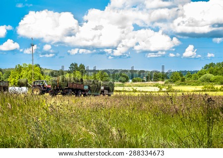 Landscape with haymaking. The tractor and the trailer of hay in a field. Fields and meadows at summer, the idyllic rural landscape and agricultural. Blue sky with clouds and sunny day.
