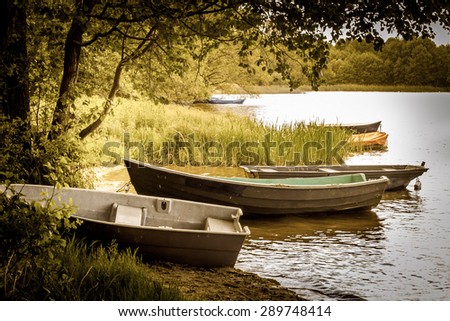 Vintage photo of landscape with moored boats for fishing on the lake at the shore. Summer holiday and vacation, leisure and relax. Nature background, vintage effect and vignette.