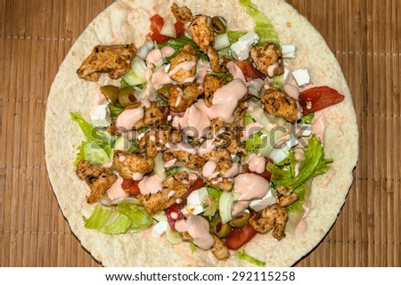 Tortilla with grilled chicken and vegetables on bamboo mat background