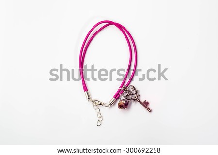 Close-up of handmade bracelet made with pink leather, crystal glass and pendant in shape key isolated on white background, top view.
