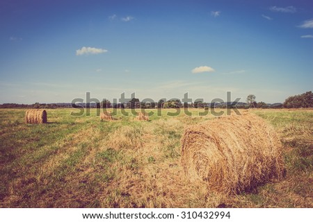 Vintage landscape showing straw bales on stubble field. Agricultural or rural landscape in summer photographed in Poland.
