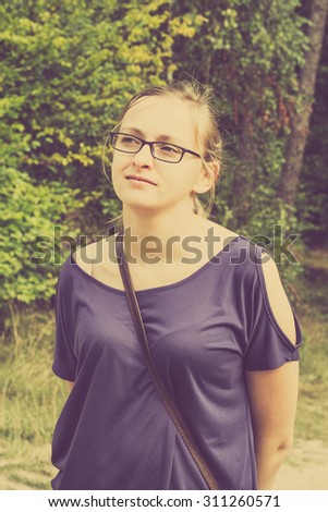Vintage portrait of attractive woman blonde, who has glasses on face. Nature in the background.