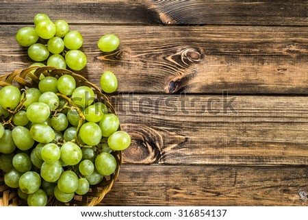 Bunch of green grapes in the basket, fruits of autumn, a symbol of abundance on rustic wood background with copy space, top view, close-up.