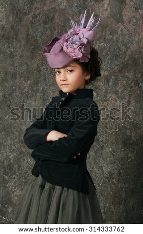 Elegant little girl 8-9 years old wearing  trendy jacket and elegant hat posing over dark wall
