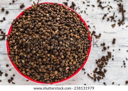 Black peppercorns in red ceramic bowl on wooden white background