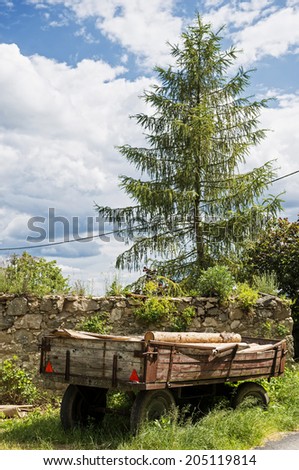 tap line behind the tractor loaded with timber standing in the grass near a stone wall and tree