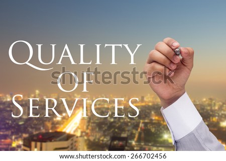 Business man\'s hand writing massage quality of services at transparent board on blurred night city background