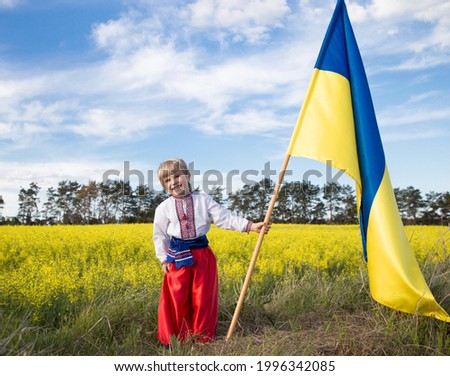 Smiling boy in national Ukrainian clothes with yellow - blue large flag in hand against background of blooming rapeseed field. pride, symbol of country, nationality of Ukraine. Patriotic education. Сток-фото © 