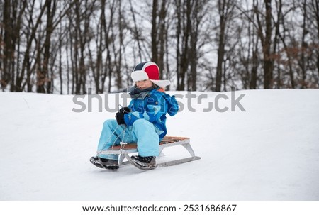 Foto Bild Ein Junge in leuchtend oranger Jacke und gelber Mütze hält einen gekauften Weihnachtsbaum in den Händen, lächelt und schaut in die Ferne. Einkaufen für die Feiertage. Vorbereitungen für Weihnachten, Neujahr