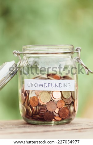 Money jar full of coins with the word crowdfunding on it.