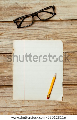 A blank old piece of paper on a wooden desktop with a pen and horn-rimmed glasses.