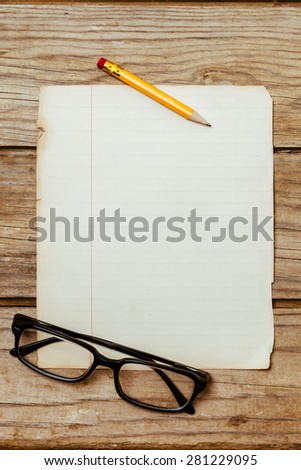 A blank old piece of paper on a wooden desktop with a pen and horn-rimmed glasses.