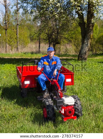 farmer in blue overalls controls motor-block. red trailer