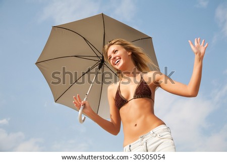 Blond woman in bikini relaxing (sunbathing) under an umbrella on the beach