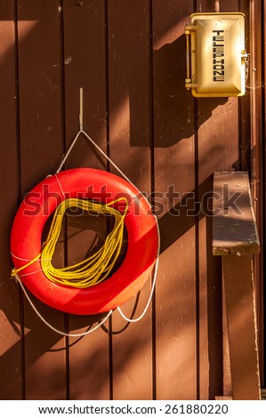 A life saver ring hangs next to a phone box on a brown wood wall.