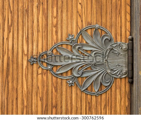 An ornate door hinge on an oak door.
