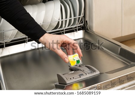 Putting tab into full integrated dishwasher close up. dishwasher machine full loaded. woman hand holding dishwasher detergent tablet.