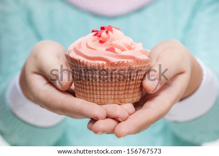 Young woman holding a pink cupcake decorated with hearts, isolated on white background