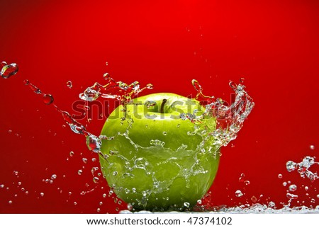 Green apple with water splash on red background