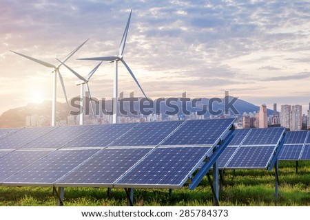 solar panels and wind turbines under sky and clouds with city on horizon. Sunrise
