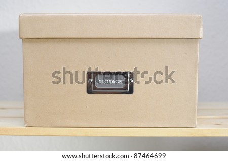 Cardboard storage box on shelf against plain wall.