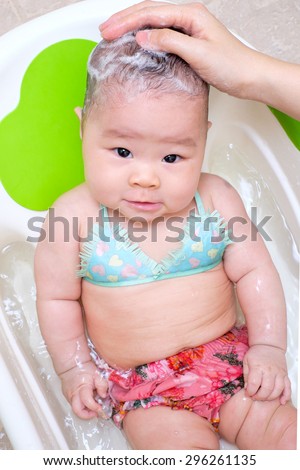 Mom washing baby girl hair, her baby in bikini, in the white tub.