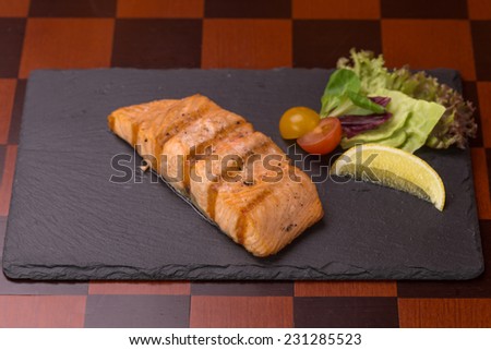 Grilled salmon steak with lemon and vegetables on wooden table at the bar