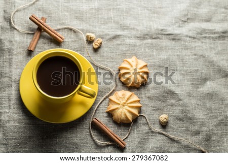 Black coffee in yellow cup with cookies and cinnamon sticks on grey fabric background