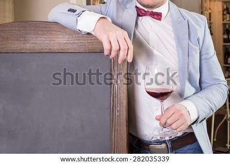 Man in suit and bow tie holding glass of red wine standing next to chalkboard
