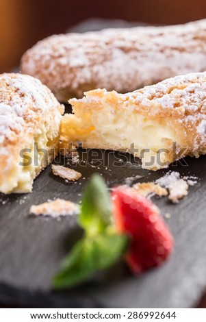 Creamy eclair dessert with strawberry on stone plate on wooden table
