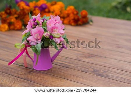 bouquet of flowers in a decorative watering can, on a wooden background