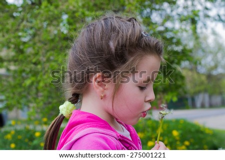 fun and funny little girl in a pink jacket holding dandelion and blowing it