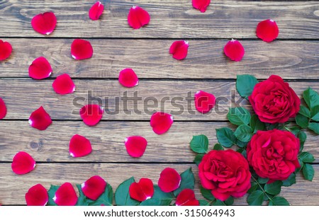 Three red roses and rose petals on the wooden background with a place for inscription