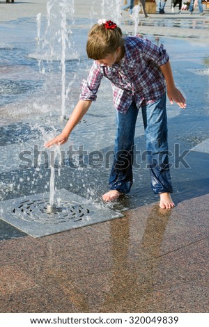 little girl 8 years in wet jeans and shirt playing in the fountain in the summer park