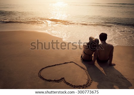 Couple sitting at the beach He was drawing a heart on the sand. During the summer