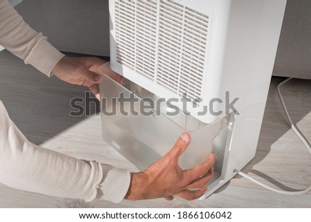 Man changing water container in air dryer, dehumidifier, humidity indicator. Humid air at home.