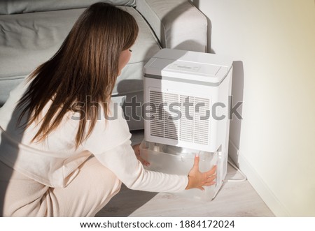 Woman changing water container in air dryer, dehumidifier, humidity indicator. Humid air at home. 